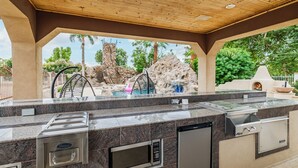An outdoor kitchen area with a stone waterfall feature, a grill, and a built-in microwave. - YNotStay_GilbertAZ - Spacious Gilbert Getaway Private Pool Home Retreat (Gilbert)