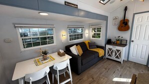En kompakt opholdsstue med spiseplads, sofa, en guitar og en dør med et skilt.