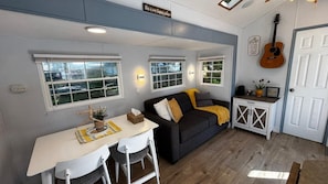 A compact living space with a dining area, a sofa, a guitar, and a door with a sign. - Family Retreat | Pool, Hot tub and Lake Access (Lindell Beach)