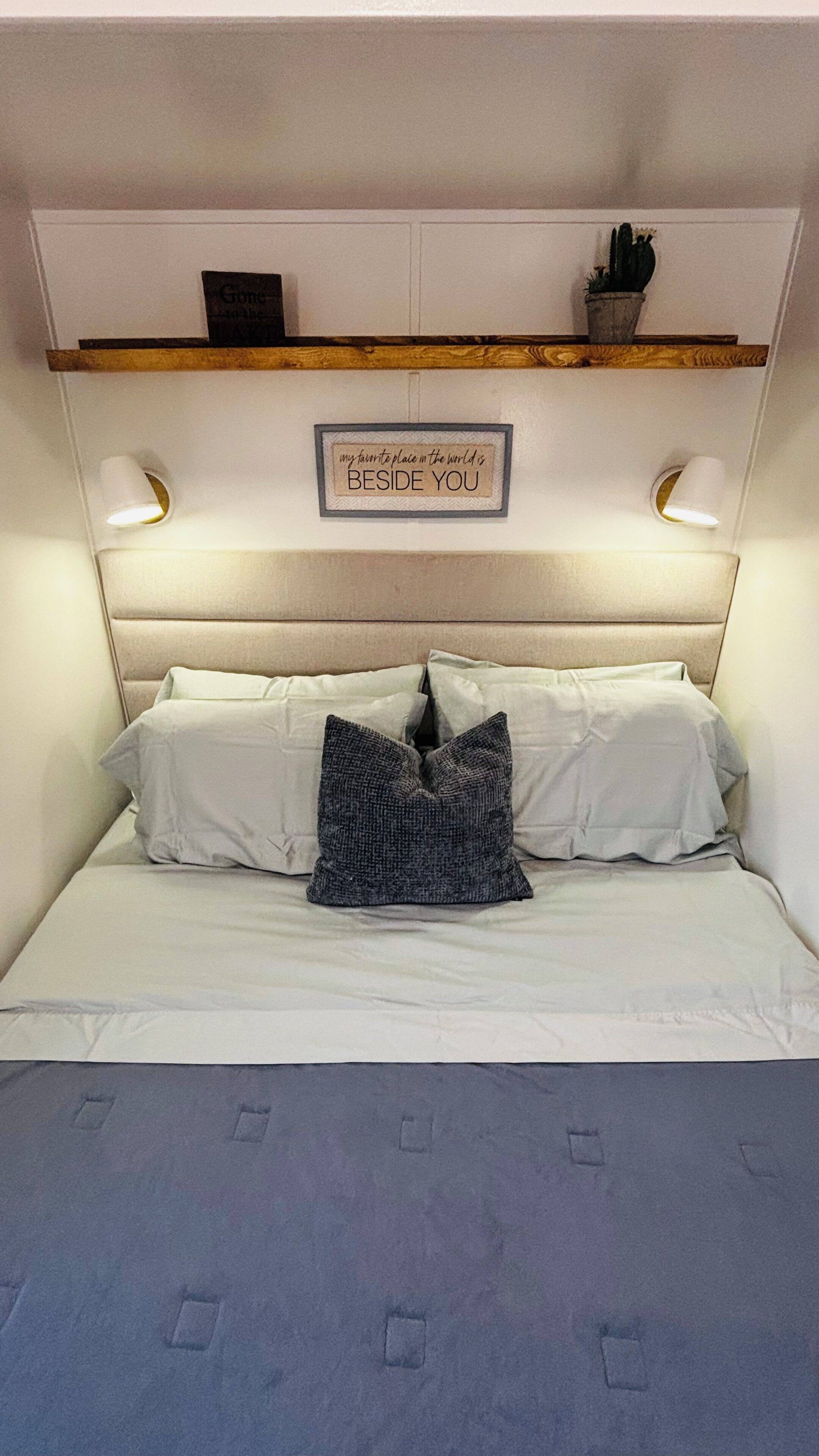 A bed with white bedding, a grey pillow, and a framed quote on the headboard.