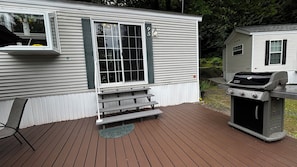 A deck with a grill and a chair, a house with a number 95 sign, and a smaller house in the background. - Family Retreat | Pool, Hot tub and Lake Access (Lindell Beach)