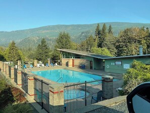 En swimmingpool med ett inhägnat område, solstolar och en byggnad med en skylt.