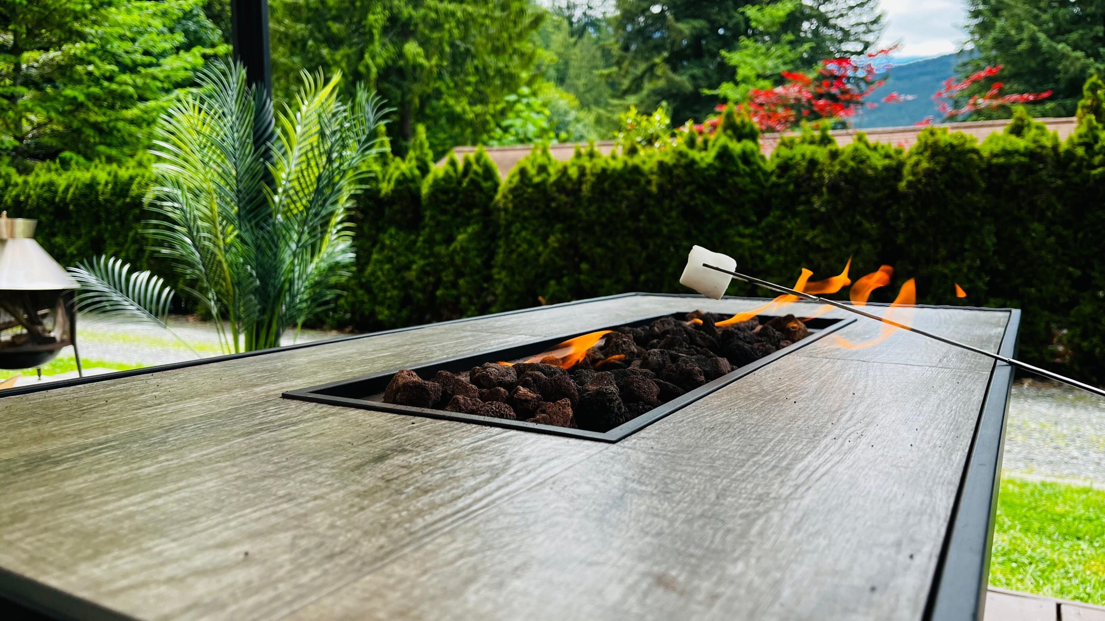 A charcoal grill with a marshmallow on a stick, surrounded by greenery.