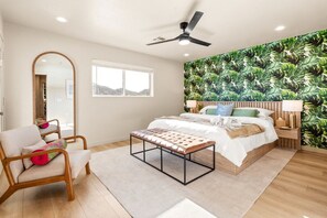 A bedroom with a bed, a chair, a bench, a ceiling fan, a window, and a wall with a leafy pattern. - Palm 2 - River Views, Private Dock & Boat Launch (Parker)