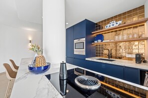 A modern kitchen with a black induction cooktop, a built-in oven, and a blue backsplash. - La Vida Mar - Luxury Sea-View Apartment Nerja with Private Terrace (Nerja)
