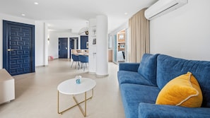Un salon moderne avec un canapé bleu, une table basse ronde et, au fond, un coin repas.