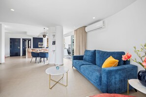 Un salon moderne avec un canapé bleu, une petite table ronde et, au fond, un coin repas.