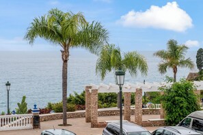 A coastal view with palm trees, a stone pergola, and parked cars. - La Vida Mar - Luxury Sea-View Apartment Nerja with Private Terrace (Nerja)