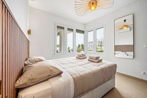 Een moderne slaapkamer met een groot bed, meerdere ramen, een houten hoofdeinde en een spiegel aan de muur.