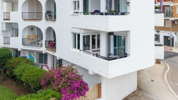 Een meerlaags gebouw met balkons, grote ramen en een tuin met roze bloemen.