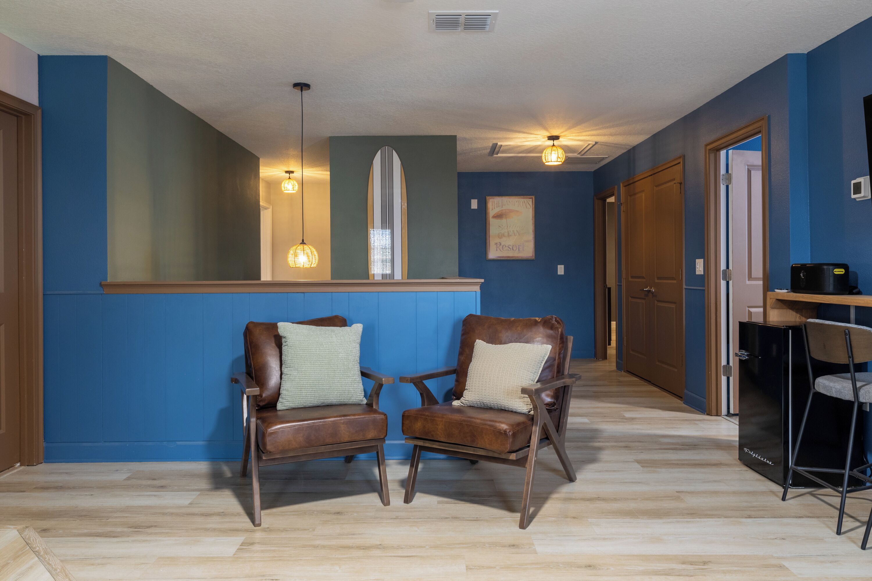 A room with two leather chairs, a wooden bench, a small table, and a black refrigerator.