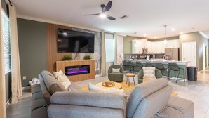 Ein modernes Wohnzimmer mit Flachbildfernseher, bequemen Sitzmöglichkeiten, einem Kamin und einer Küchenzeile mit Barhocker.