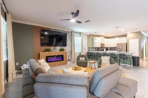Ein modernes Wohnzimmer mit Flachbildfernseher, bequemen Sitzmöglichkeiten, einem Kamin und einer Küchenzeile mit Barhocker.