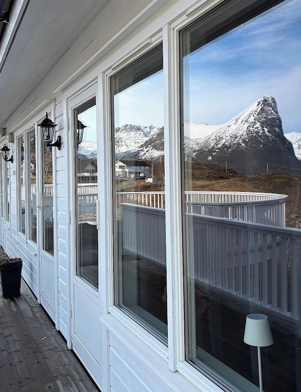 A covered porch with large windows overlooking a snowy mountain.
