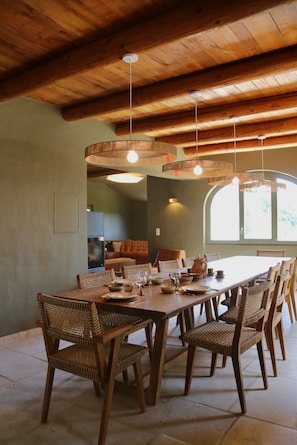 A dining area with a wooden table and chairs, hanging light fixtures, and a view of the outdoors through a window. - Mas d'âme-Gîte d'exception with swimming pool between sky and hills in Haute Provence (REVEST SAINT MARTIN)
