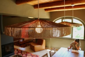A room with a hanging woven light fixture, a wooden ceiling, and a view through a window.