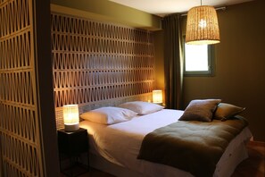 A bedroom with a bed, two bedside lamps, a window, and a decorative wall panel. - Vrbo Property (REVEST SAINT MARTIN)