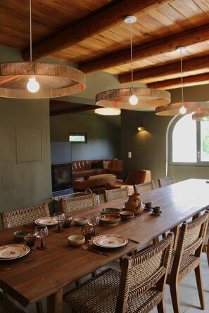 A dining area with a long wooden table set for a meal, wicker chairs, and hanging wicker light fixtures. - Vrbo Property (REVEST SAINT MARTIN)