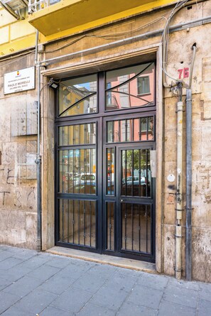 A building entrance with a large black metal gate, a plaque, and a number '76' on the wall. - Urban Retreat 76 - Two Bedroom Apartment, Sleeps 8 (Naples)