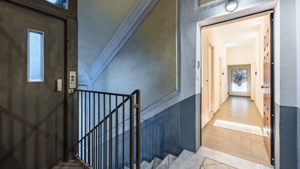 Eine Treppe mit Metallgeländer führt zu einem Flur mit Holzboden und einer Tür am Ende.