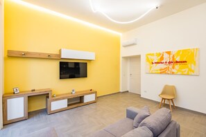 Una sala de estar moderna con una pared amarilla, un televisor montado, una mesa consola de madera, un sofá gris y un cuadro abstracto grande.