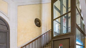 A staircase with metal railings, a door with a red emergency light, and a wall with a textured finish. - Solaris Studio - Solaris Suites (Naples)