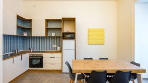 A modern kitchen with a wooden countertop, built-in oven, and white cabinetry. There is a dining table with black chairs and a yellow patterned wall art piece. - Solaris Studio - Solaris Suites (Naples)