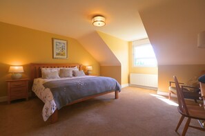 Quarto com cama, duas luminárias de cabeceira, uma janela e uma cadeira.
