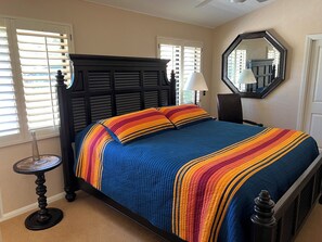 Ein Schlafzimmer mit einem Bett, einem runden Tisch, einer Lampe, einem Spiegel und einem Fenster mit Jalousien.
