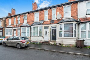 A row of terraced houses with satellite dishes, a car parked on the street, and a trash bin. - NEW! 4BR House, free parking, near City Centre (Nottingham)