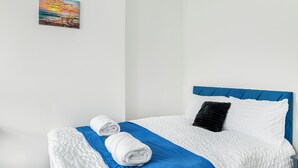 Een net opgemaakt bed met blauw-witte beddengoed, een opgerolde handdoek en een kussen.