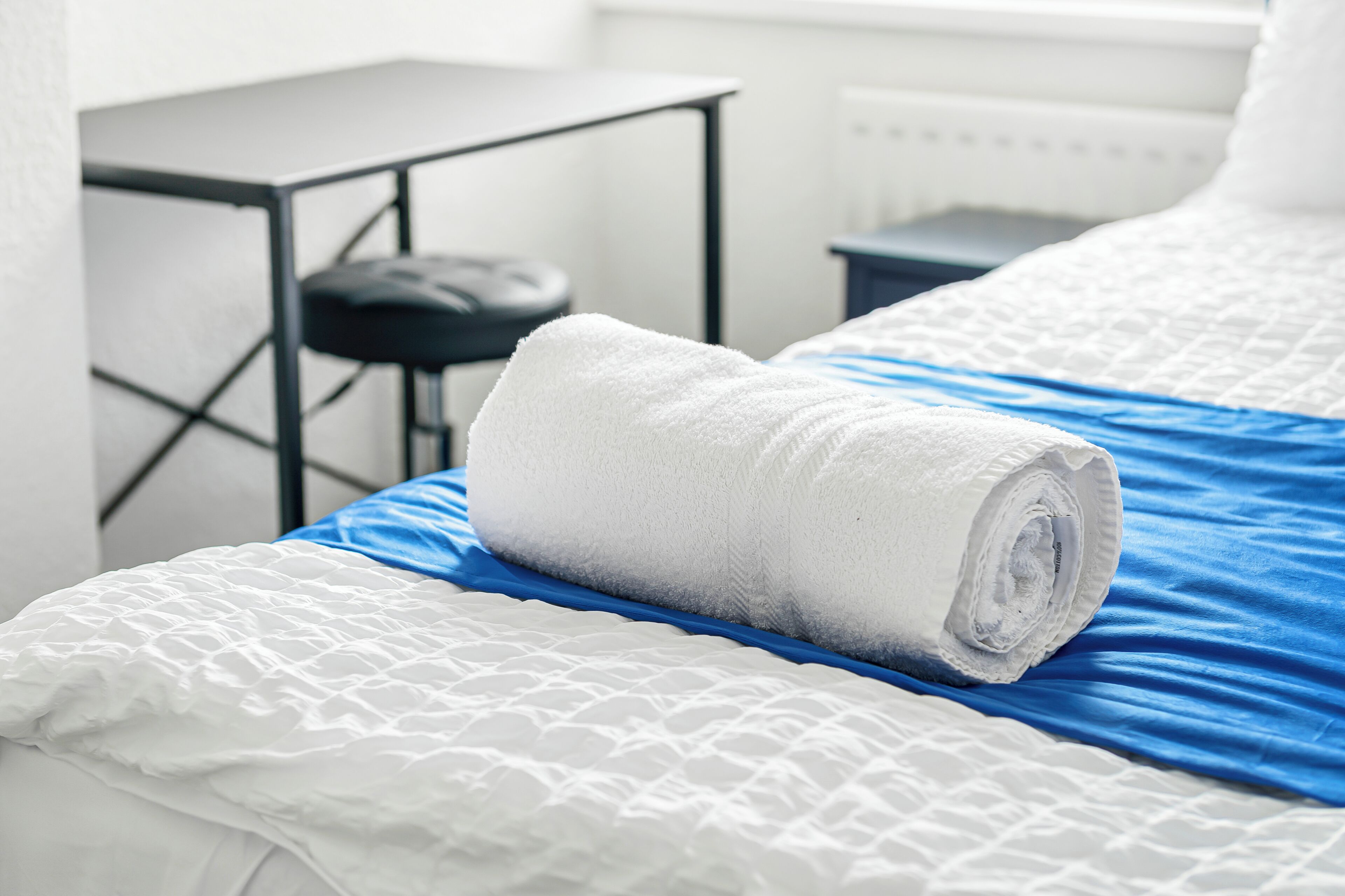 Un lit bien fait, avec une serviette blanche enroulée, une couverture bleue et un oreiller blanc à texture.