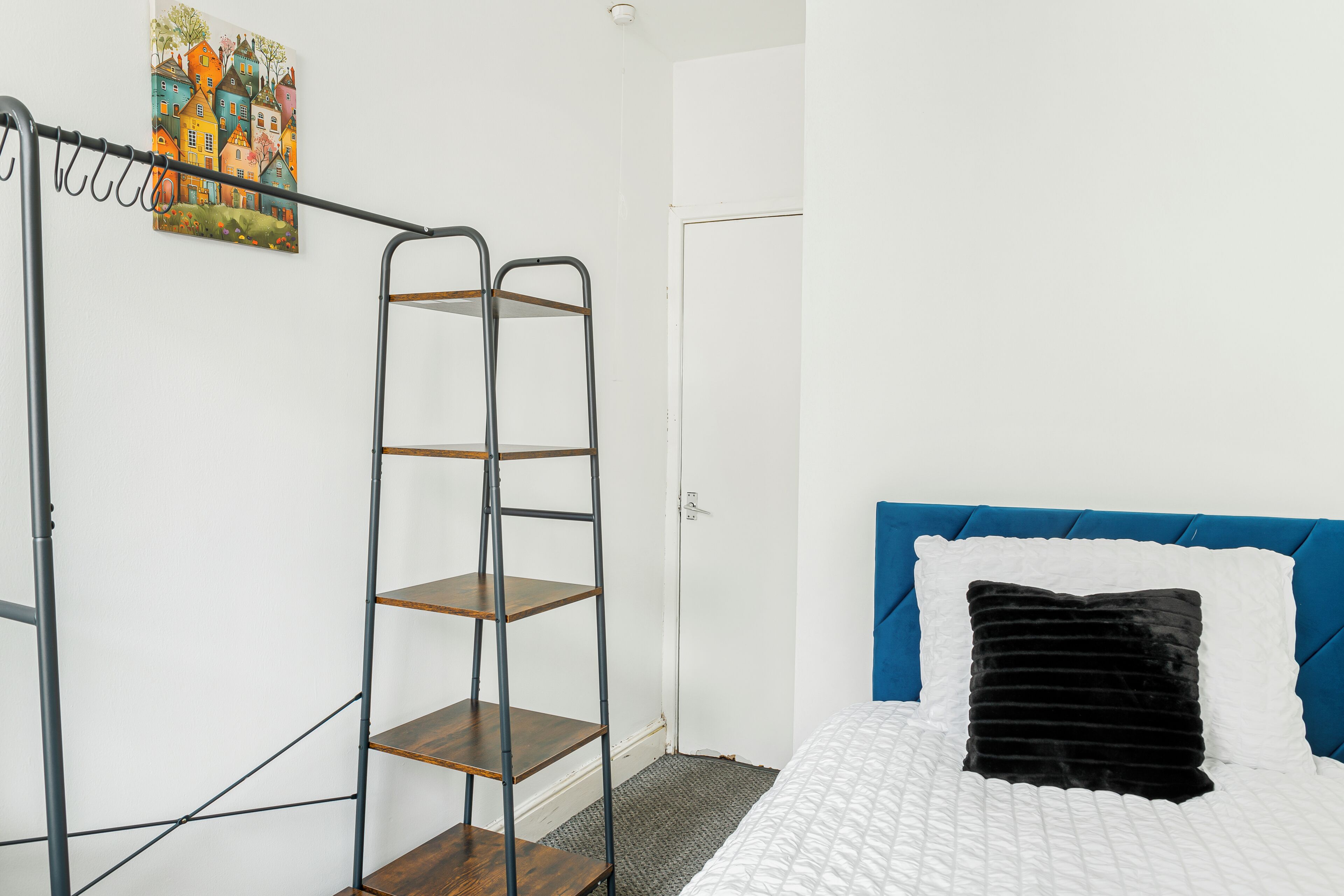 A bedroom with a bed, a blue headboard, a black pillow, a white pillow, a wooden ladder, and a door.
