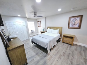 A bedroom with a bed, bedside tables, a ceiling fan, and a door leading to another room. - Guest house pine ridge 2nd floor unit over shop. (Naples)