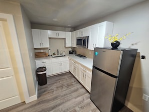 A compact kitchen with white cabinets, a stainless steel refrigerator, a microwave, and a sink. - Guest house pine ridge 2nd floor unit over shop. (Naples)