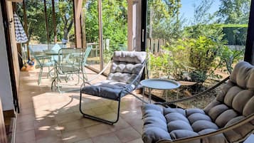 Eine überdachte Terrasse mit gepolstertem Stuhl, einem kleinen Tisch und einem Glastisch-Set.