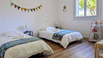 Ein Zimmer mit zwei Betten, einem Fenster mit Blick auf Bäume, einer an der Wand hängenden Uhr und einem kleinen Tisch mit einer Lampe.