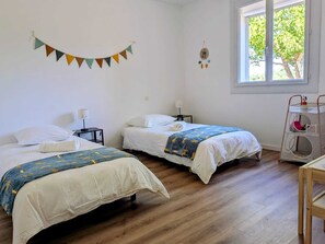 Une chambre avec deux lits, une fenêtre donnant sur des arbres, une horloge murale et une petite table avec une lampe.
