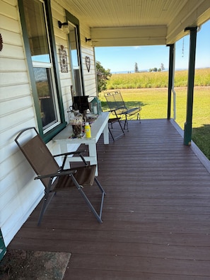 A covered porch with a table and chairs, a window, and a view of a field.
