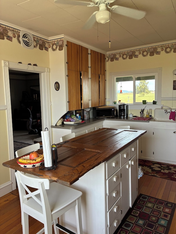 A kitchen with a wooden island, white cabinetry, a ceiling fan, and a view of a green landscape through a window.