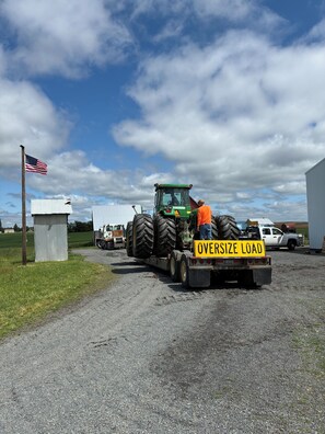 A tractor with a trailer labeled 'OVERSIZE LOAD' parked on a gravel path.