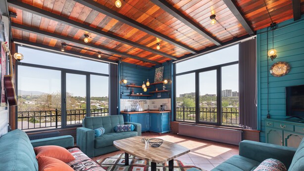 A spacious living area with large windows, a kitchen, and a balcony with a view.