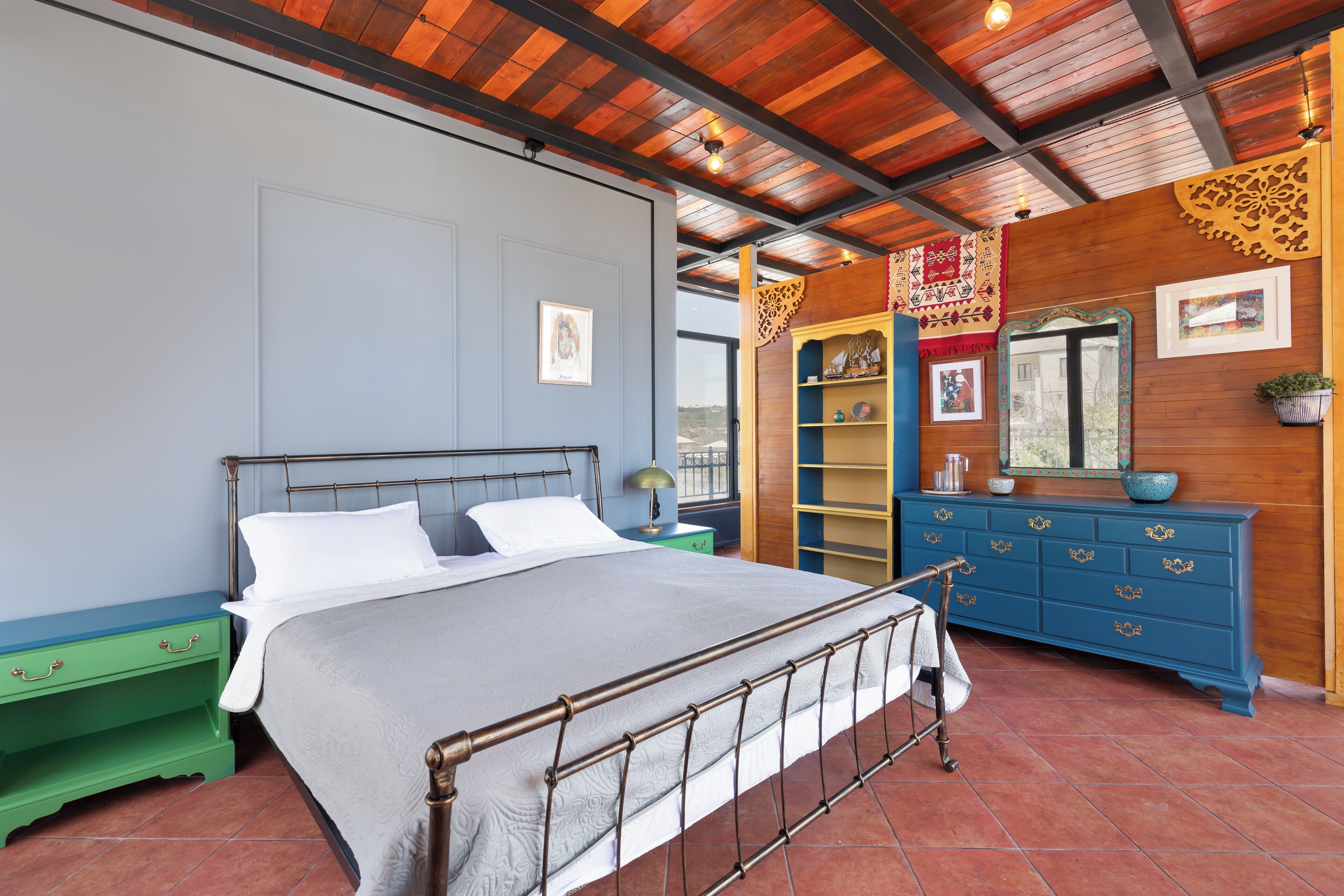 Una camera da letto con una struttura del letto in metallo, un comodino verde, una cassettiera blu e una parete in legno con elementi decorativi.