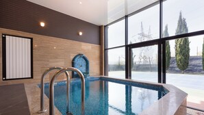 A modern indoor swimming pool with clear glass walls, a tiled floor, and a metal ladder.