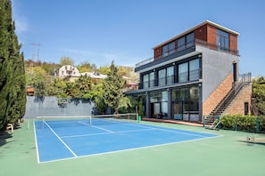 Una cancha de tenis con red, un edificio con balcón y una escalera.