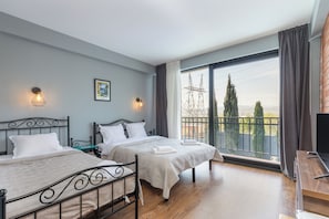 Quarto com duas camas, televisão e varanda com vista para linhas de eletricidade e árvores.