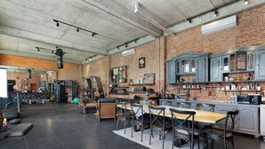 A spacious kitchen with a dining area, a workout area with gym equipment, and a brick wall.