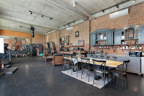 A spacious kitchen with a dining area, a workout area with gym equipment, and a brick wall.