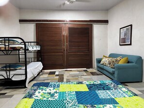 A room with a bunk bed, a blue sofa, a patterned quilt, and a large wooden door. - Delightful 1-bedroom fully equipped cabin in Nuevo Colón welcomes your stay! (Nuevo Colón)