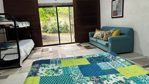 A room with a bunk bed, a sofa with floral cushions, a quilt with a patchwork design, and a door leading to an outdoor area. - Delightful 1-bedroom fully equipped cabin in Nuevo Colón welcomes your stay! (Nuevo Colón)